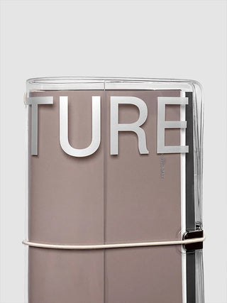 A close-up of a clear notebook cover with a taupe-brown cover inside. Large silver letters spelling 'TURE' are visible on the cover