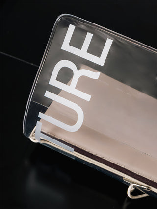 A close-up of a transparent notebook cover with large white 'TURE' lettering on a dark reflective surface.