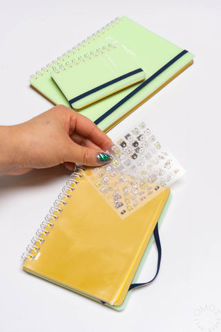 Green and yellow spiral notebooks with sticker sheet and hand