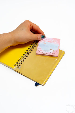Cream spiral notebook with hand, open pages, and a pink note card