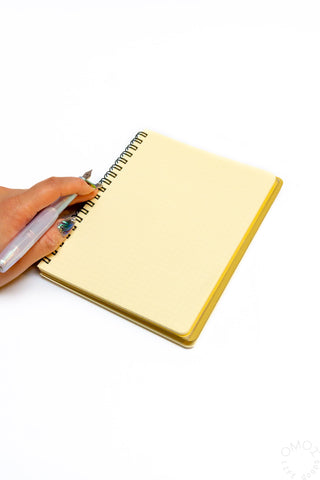 Cream spiral notebook with hand at the spiral binding and dark blue elastic band