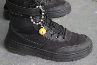 Black boot with a chain and yellow charm on a gray surface
