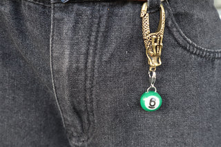 Gold keychain with a green pool chain charm attached to denim pants.