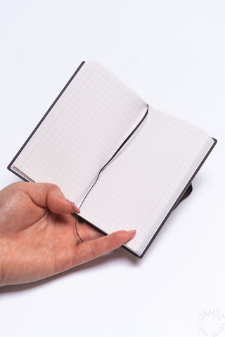 Hand holding a white grid notebook with notebook string on a white background