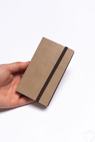 Hand holding a brown notebook with a dark brown strap on a white background
