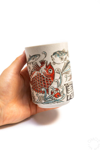 Fish teacup held in hand, cream ceramic with colorful fish and symbols