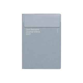 A light gray planner with a matching flap closure on the cover, featuring white text that reads 'Une Semaine Journal Intime 2027' on a plain white background.