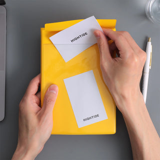A person's hands holding a bright yellow planner with a pocket placing white cards labeled 'HIGHTIDE' inside.