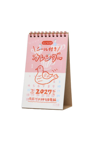 A Japanese desk calendar for 2027 with a pink and white cover featuring a bird illustration and Japanese text, shown standing on a white background.