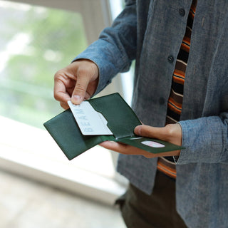 Person holding a green wallet with a card inside, blurred background