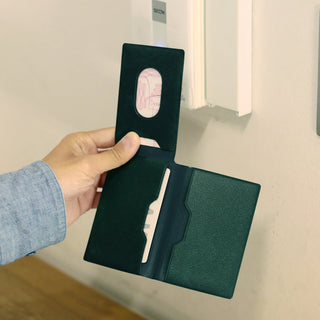 Hand holding a green card case with cards inside, against a neutral background.
