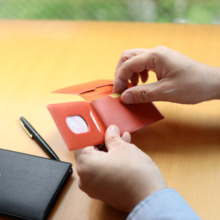 Person opening a small orange wallet on a wooden surface with a blurred natural background