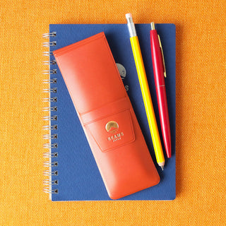 Orange pen case next to writing utensils on a blue notebook against an orange background