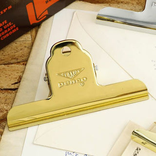 Gold steel binder clip on an envelope and papers, close-up view