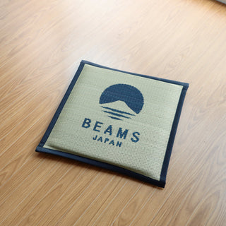 Beams Japan logo on a navy square cushion on a wooden surface