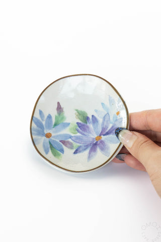 Hand holding a small ceramic dish with floral design on a white background