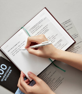 Person writing in a notebook with a pen on a light gray surface