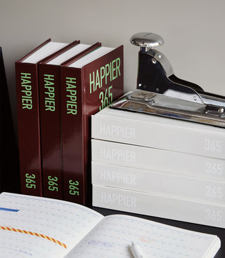 Stack of 'Happier 365' books and a stapler on a surface.