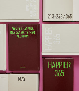 Collection of 'Happier 365' planners on a pink background