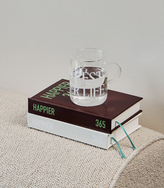 Clear mug with text on a book titled 'Happier' on a textured surface