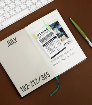Journal with a page and a receipt and polaroid taped to it, placed on a desk with a keyboard and pen.