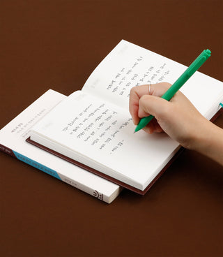 Hand writing in an open book with a green pen on a brown background