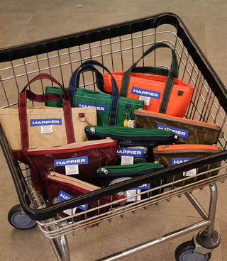 Shopping cart filled with 'Happier' branded bags on a concrete floor.