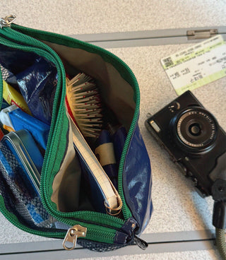 Open blue toiletry bag with green zipper on a surface next to a camera and passport.