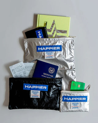 Collection of 'Happier' pouches with various items on a light gray background