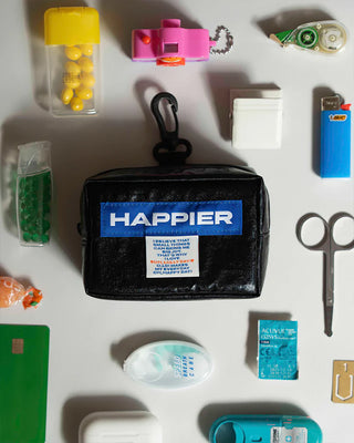 Black pouch with 'HAPPIER' branding surrounded by various small items on a white surface