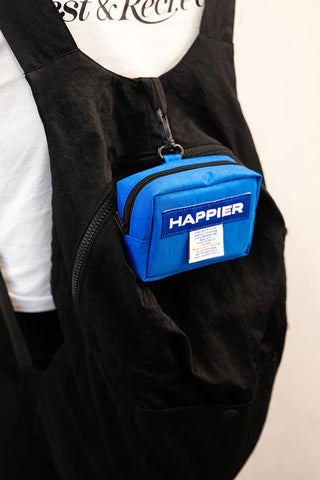 Blue bag with 'Happier' branding attached to a black backpack on a plain background