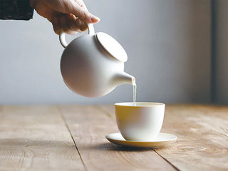 Hand holding teapot pouring tea into cup