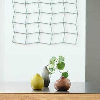 Three small ceramic vases on a table with plants inside and a geometric wall art in the background.