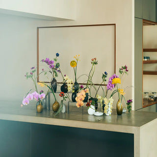 A styled arrangement of colorful flowers in various glass vases, displayed on a countertop in a modern kitchen setting.
