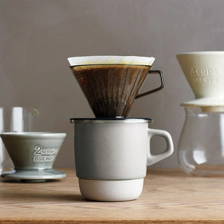 Coffee brewing setup with a pour-over coffee maker and a mug on a wooden surface.