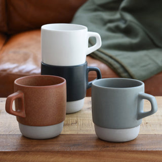Four ceramic mugs in different colors on a wooden surface with a blurred background.