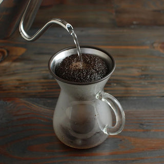 Coffee being poured into a glass coffee carafe on a wooden table