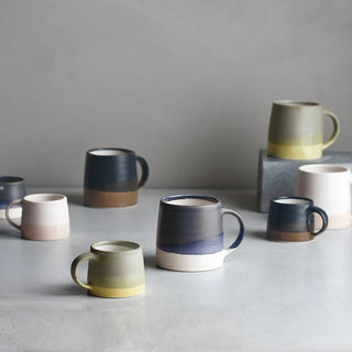 Set of ceramic mugs in various colors on a gray surface with a neutral background