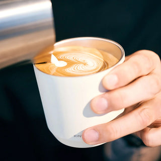 Hand holding a white tumbler pouring latte art