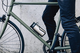 Person sitting on a green bicycle with a thermos attached, against a concrete wall.