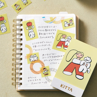 Stamp-style translucent washi tape strips with character figures beside a notebook