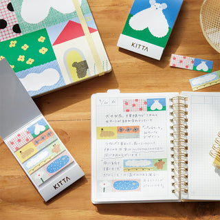 Kitta sticker books on a wooden surface with an open notebook displaying stickers.