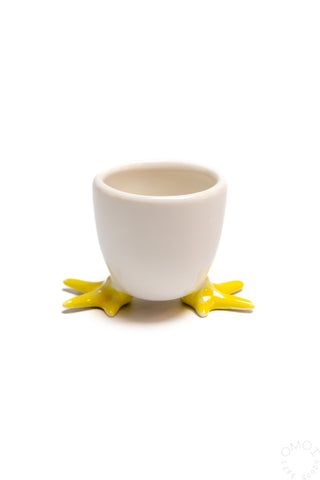 A white ceramic egg cup with yellow feet at the base on a white background.