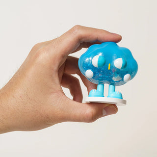 Hand holding a small blue and white toy figure against a light background