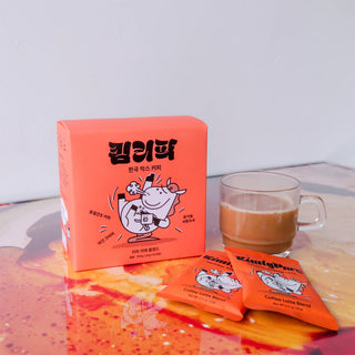 Orange packaging of a KimlyParc product with a cartoon cow design, next to a glass of coffee.