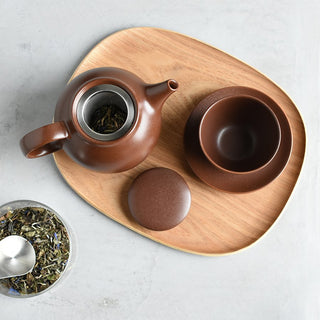 Top view of opened teapot with tea leaves and tea set on wooden tray