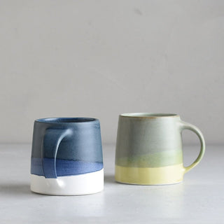 Two ceramic mugs, one blue and white, the other green and yellow, on a light gray background.