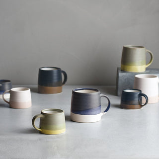 Set of ceramic mugs in various colors on a gray surface with a neutral background