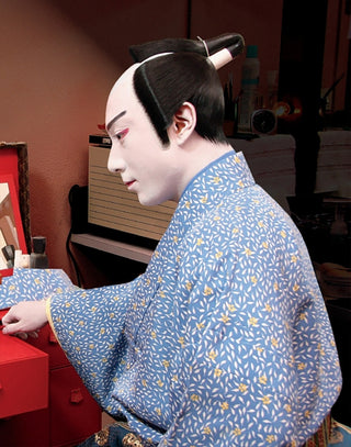 Person in traditional Japanese costume with a blue patterned kimono, sitting in a room.