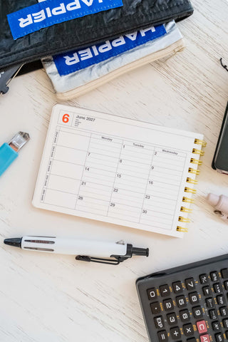 Opened small notebook calendar with stationery items scattered around a table